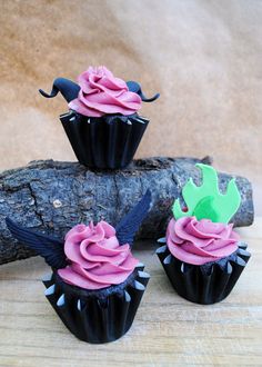 three cupcakes with pink frosting and green icing sitting on a piece of wood