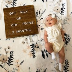 a baby laying on top of a bed next to a sign that says get milk or cry trying 2 months