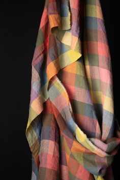 a multicolored checkered scarf hanging on a black background with the fabric pulled back