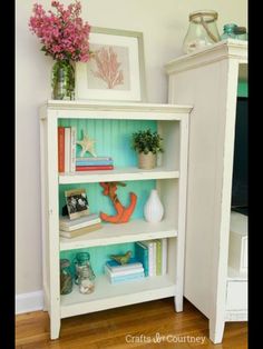 a white book shelf filled with books next to a vase and pictures on the wall