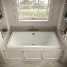 a bath tub sitting under a window next to a shelf filled with bottles and vases