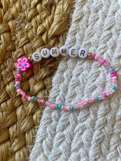 a bracelet that says summer with flowers and beads on the end, sitting on a woven surface