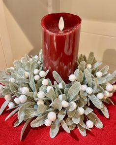 a red candle sitting on top of a table next to a bunch of greenery