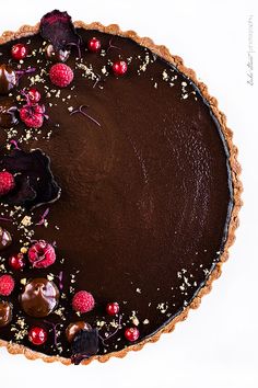 a chocolate tart topped with raspberries and other toppings on a white surface