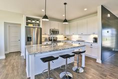 a large kitchen with white cabinets and marble counter tops, two bar stools in front of the island