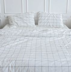 an unmade bed with white sheets and black checkered comforter on the headboard