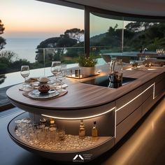 a counter with wine glasses and plates on it in front of a window overlooking the ocean