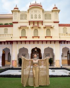 a woman standing in front of a white building holding a tan sari over her shoulders