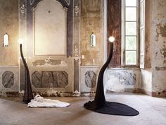 two black sculptures in an old room with light coming from the windows and floor lamps on either side