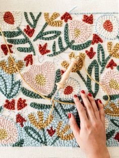 a woman's hand is stitching on a rug with a needle and thread