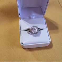 an engagement ring in a white box on a brown tableclothed surface with a gold and silver band around it