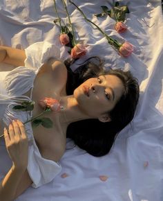 a woman laying on top of a bed with pink roses in her hair and wearing a white dress