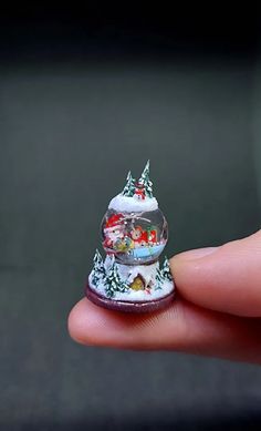 a hand holding a small snow globe with christmas decorations on it's top and bottom