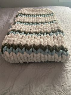 a crocheted blanket sitting on top of a bed next to a white pillow