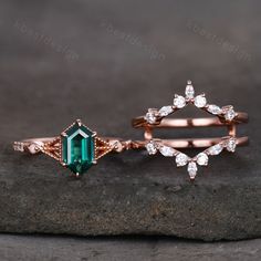 two rings with emerald and white diamonds on them sitting on a black rock next to each other