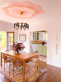 a dining room table with chairs and flowers on it in front of an open kitchen door