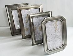 three silver frames sitting next to each other on a white tablecloth covered surface, with one empty frame in the middle