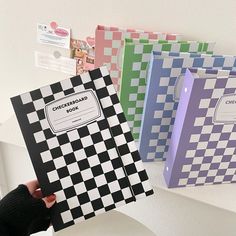 a person holding three notebooks in front of a wall with checkered paper on it