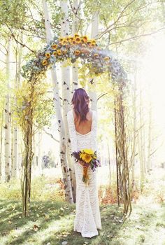 a woman standing in front of a tree with sunflowers on her wedding dress