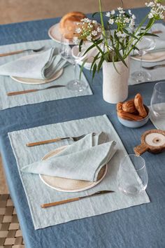 a table set with place settings and flowers in a vase on the top, along with napkins