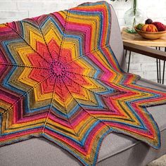 a crocheted blanket on a couch in front of a table with fruit and vases