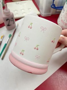 a person is holding a paper cup with cherries and bows on it, next to other crafting supplies