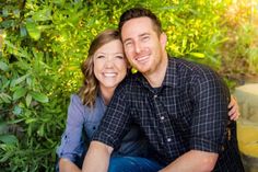 a man and woman sitting next to each other in front of some trees with leaves