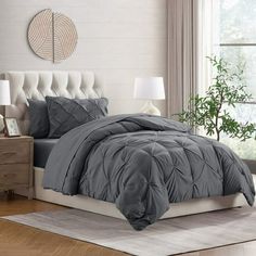 a bed with grey comforter and pillows in a room