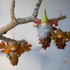 three pine cones hanging from a tree with two gnomes on them and one is holding an acorn