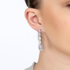 Step into a world of glamour with the Crawford Drop Earrings in Silver White. Exquisitely fashioned  and resplendent with dazzling simulated diamonds, these earrings exude an Art Deco charm that’s both vintage and timeless.  The elegant drop design features five rectangular settings. Each setting is graced with a unique arrangement of gemstones, crowned by a single radiant simulated diamond at the bottom, encircled by a stunning array of baguette-cut stones.   These earrings are designed for bot Luxury Sparkling Diamond Earrings For Formal Occasions, Luxury Baguette Diamond Earrings For Formal Events, Luxury Wedding Linear Earrings For Pierced Ears, Glamorous Brilliant Cut Diamond Earrings For Evening, Luxury White Linear Earrings For Formal Occasions, Luxury Bridal Drop Earrings With Diamond Accents, Luxury Baguette Cut Bridal Earrings, Luxury Linear Earrings With Prong Setting For Formal Events, Luxury Brilliant Cut Linear Earrings For Formal Occasions