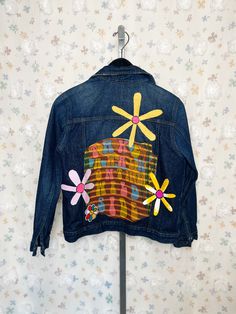 a denim jacket with flowers painted on it hanging from a clothes hanger against a wall