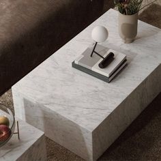 a marble coffee table with a book, vase and lamp on the end shelf next to it