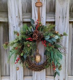 a wreath hanging on the side of a wooden door with a bell and evergreens