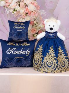 a teddy bear sitting on top of a table next to two pillows and a bouquet