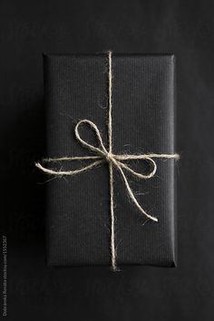 a black wrapped gift box with a white string tied around it on a black background