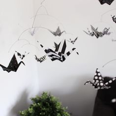 black and white origami butterflies are hanging from the ceiling above a table with a potted plant