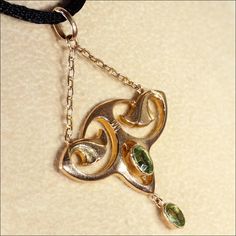 "This gorgeous Art Nouveau pedant has a touch of Egyptian revival flare. With it's floral motifs and bright sparkling spring green Peridot gems, this lovely piece has wonderful lines that make me long for warm days in the garden. This hand crafted pendant was made in England in about 1900. The two peridots add up to about .65 carats. The pendant measures 46.2 mm across and 32.2 mm top to bottom (26.8 mm not including the chain), it weighs 1.6 grams. Thanks! If you like this piece and would like Art Nouveau 14k Gold Jewelry With Gemstones, Art Nouveau Yellow Gold Jewelry For Anniversary, Art Nouveau Pendant Jewelry With Intricate Design, Yellow Gold Art Nouveau Jewelry For Anniversary, Elegant Yellow Gold Jewelry With Historical Design, Elegant Green Engraved Jewelry, Art Nouveau 14k Gold Jewelry For Anniversary, Art Nouveau Jewelry With Historical Design As Gift, Art Nouveau Jewelry With Historical Design For Gift