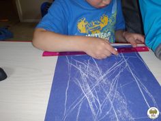 a young boy is drawing on a piece of blue paper with white crayons