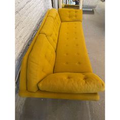 a yellow couch sitting in front of a brick wall next to a mirror on the floor