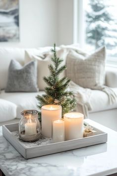 candles and a christmas tree on a tray in front of a couch with white pillows