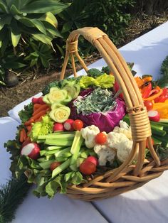 a basket filled with lots of vegetables sitting on top of a white table covered in greenery