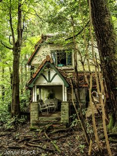 an old house in the woods with chairs and tables on the outside, surrounded by trees