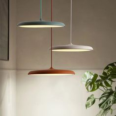 three hanging lights above a table with a plant in the corner and a potted plant next to it