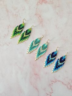 three pairs of beaded earrings sitting on top of a marble counter next to each other