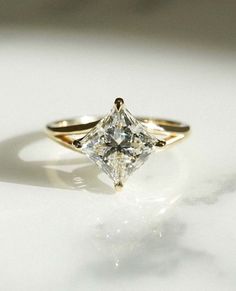 a yellow gold engagement ring with a princess cut diamond in the center on a white surface