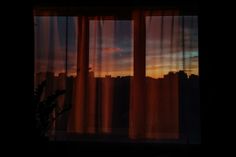 the sun is setting behind some curtains in front of a window with cityscape