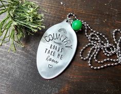 a metal spoon with a green bead hanging from it's side on a wooden table