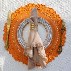 an orange plate topped with a napkin and gold fork, knife and spoon rest on top of it