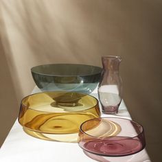 three different colored glass bowls sitting on top of a white table next to a vase