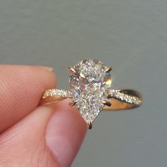 a person holding a ring with a pear shaped diamond in it's center and side stones on the band